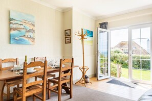 A dining area with wooden furniture, a painting on the wall, and a view through a glass door.