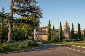 Un bâtiment historique en pierre, doté d’une tour, entouré d’une pelouse bien entretenue et de grands arbres.