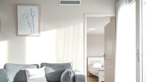 Un salon moderne avec un canapé gris, une œuvre d’art encadrée et un lit à l’arrière-plan.