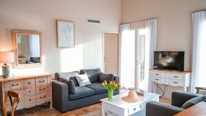 Un salon avec un canapé gris, une table basse blanche, un téléviseur posé sur un meuble en bois, un miroir et un tableau encadré accroché au mur.