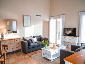 Un salon avec un canapé gris, une table basse blanche, un téléviseur posé sur un meuble en bois, un miroir et un tableau encadré accroché au mur.