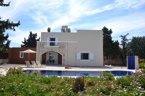 Une maison à deux étages dotée d’une piscine, d’une arche en pierre et d’un espace extérieur aménagé pour se détendre.
