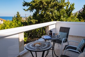 Un balcon avec deux tables et des chaises, une vue sur la mer et un grand arbre.