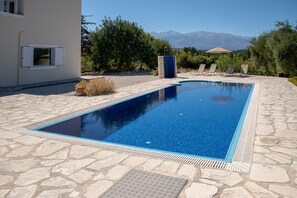 Une piscine rectangulaire bordée de pierres, entourée d’une terrasse aménagée avec des chaises longues et offrant une vue sur les montagnes.