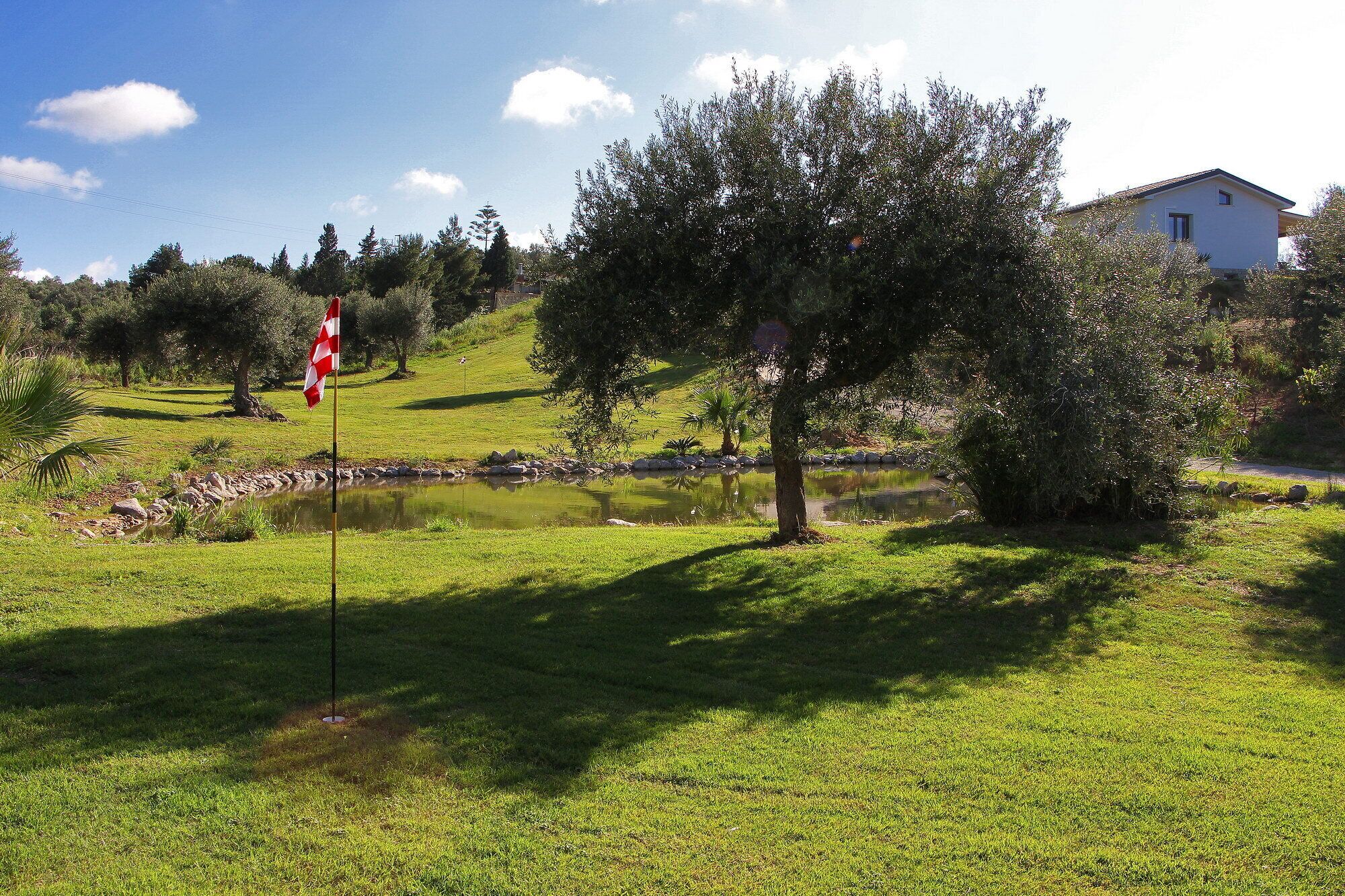 Un terrain de golf avec un drapeau, un étang et une maison en arrière-plan.