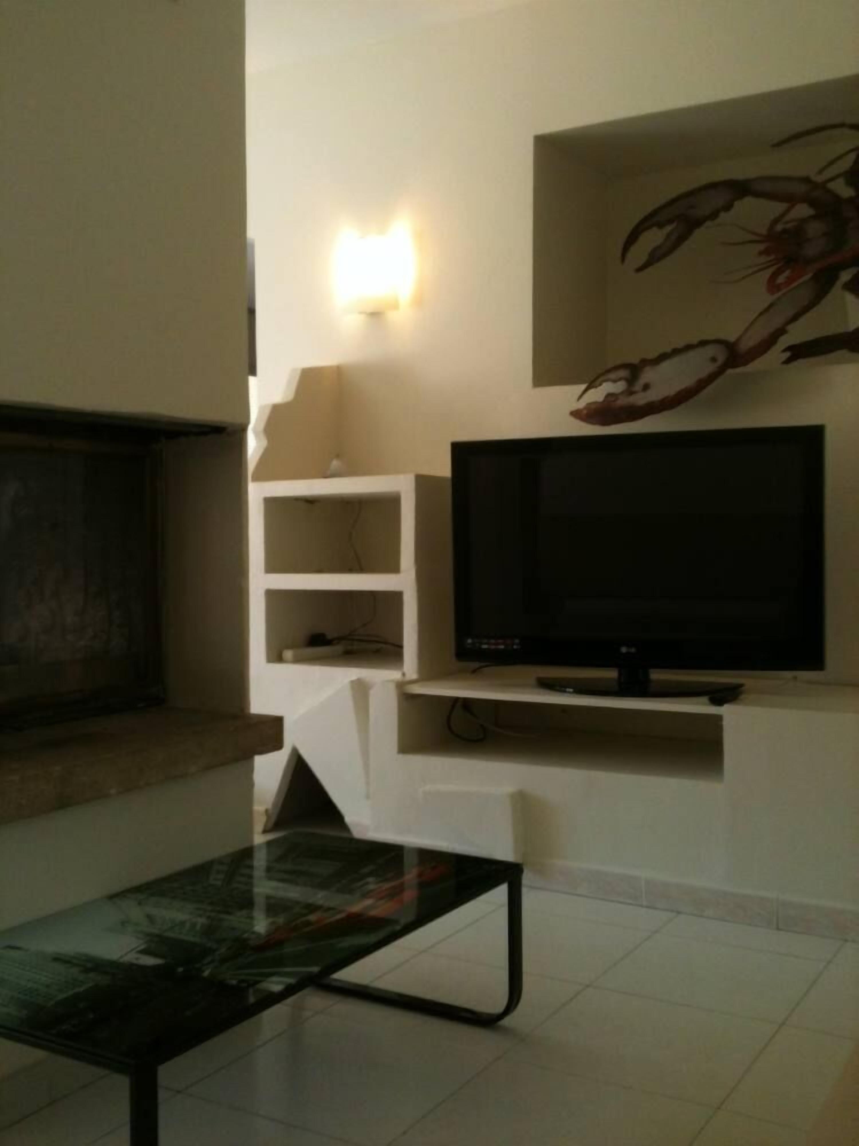 A living room with a flat-screen TV on a white stand, a glass coffee table, and a decorative wall piece.