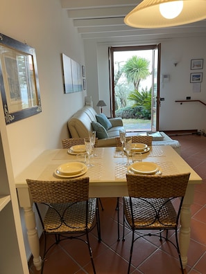 A dining area with a table set for four, surrounded by wicker chairs, a sofa, and a lamp.