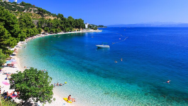 A coastal beach with clear waters, a boat, and people swimming. - Villa Oliva - exclusive gateway, luxurious serenity, stunning views, heated pool (Podgora)
