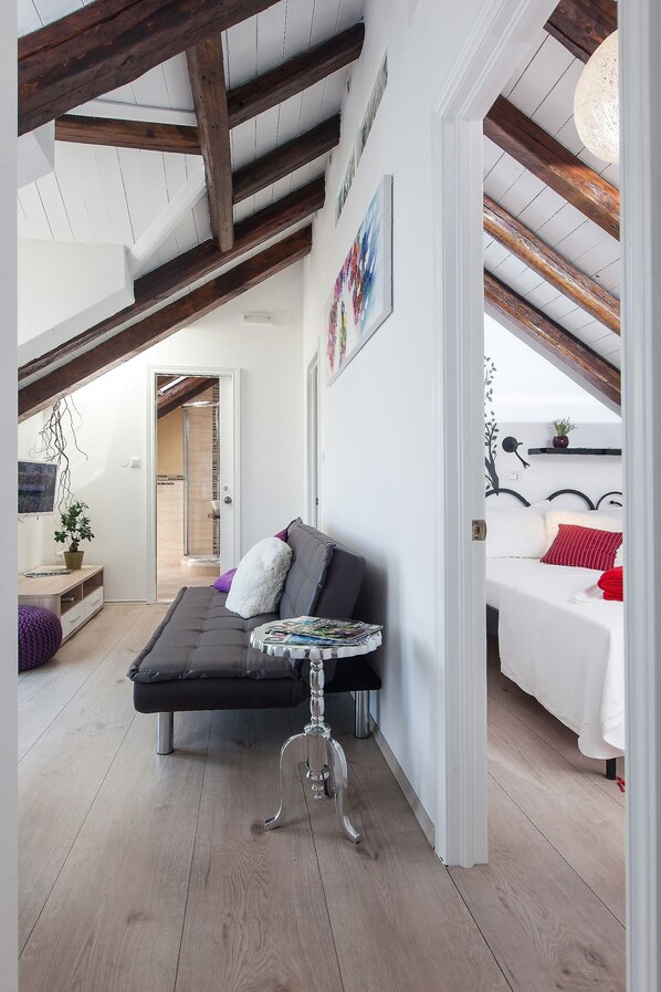 Une chambre de style loft moderne, avec des poutres en bois apparentes, un lit en mezzanine, un canapé et une petite table.