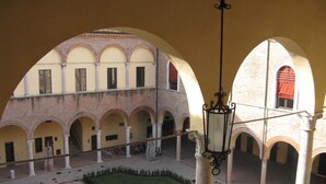 A courtyard with multiple arches, a central garden, and a hanging light fixture. - Beautiful and spacious apartment, with garage, in an ancient building in the city center.  (Ferrara)