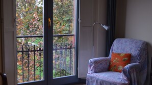 A room with a patterned armchair, a door leading to a balcony with a view of trees, and a floor lamp. - Beautiful and spacious apartment, with garage, in an ancient building in the city center.  (Ferrara)