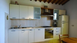A compact kitchen with white cabinets, a stove, and a refrigerator. - Detached house, stone, 6 pax, garden, wonderful sea view (Casale Marittimo)