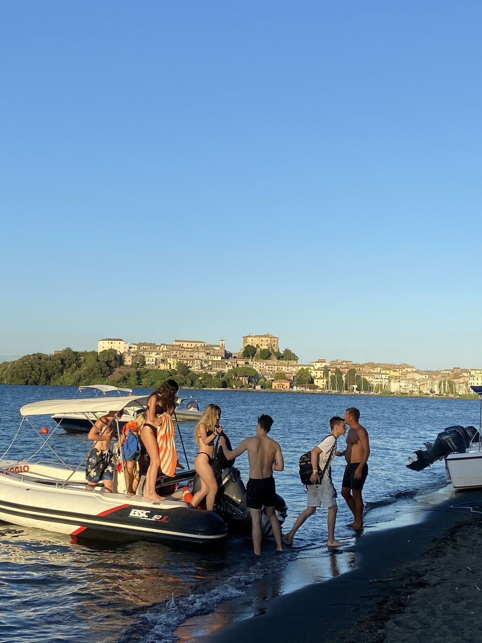 Un grupo de personas desembarca de un barco en una playa, con un edificio histórico al fondo.