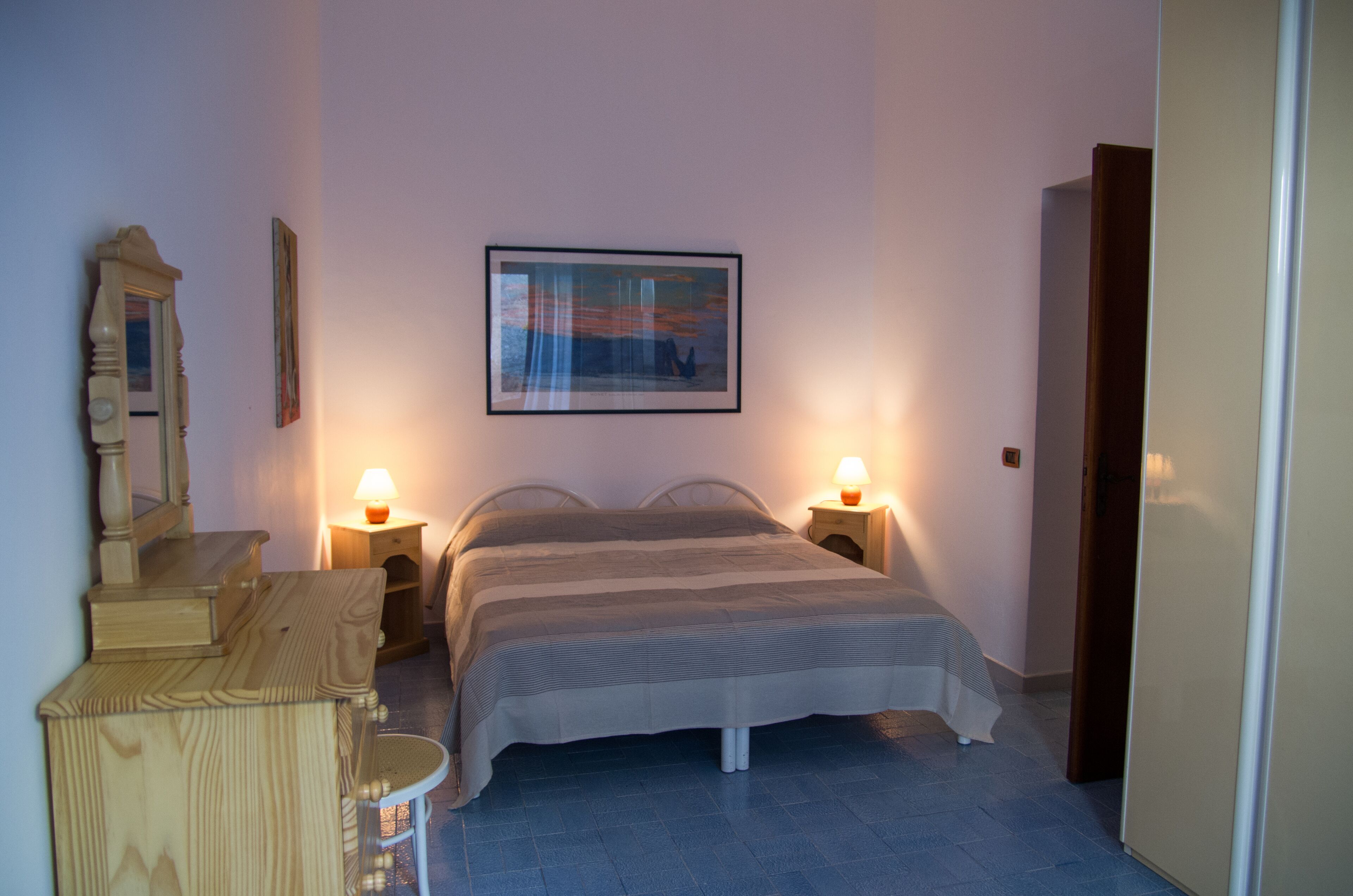 A bedroom with a bed, bedside lamps, a dresser, a mirror, and a framed picture on the wall.