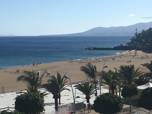 A beach with palm trees, a pier, and a mountain in the background. - Stunning front line 2 bedroom apartment (Tías)