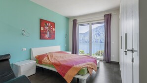 Une chambre à coucher avec un lit, une table de chevet, une chaise, un tableau et une fenêtre avec des rideaux.