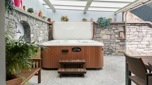 Un bain à remous situé dans un espace extérieur abrité, avec des murs en pierre, des meubles en bois et des plantes en pot.