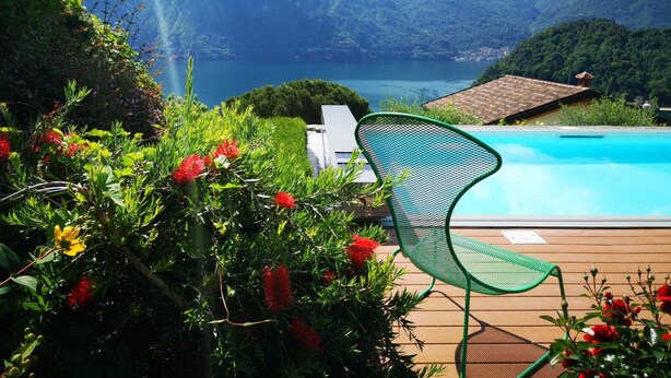 Un espace aménagé au bord de la piscine, avec un fauteuil, entouré d’une végétation luxuriante et offrant une vue sur les montagnes.
