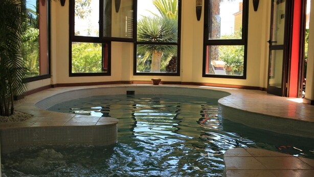 Ein Innenpool mit klarem Wasser, umgeben von gefliesten Wänden und großen Fenstern.