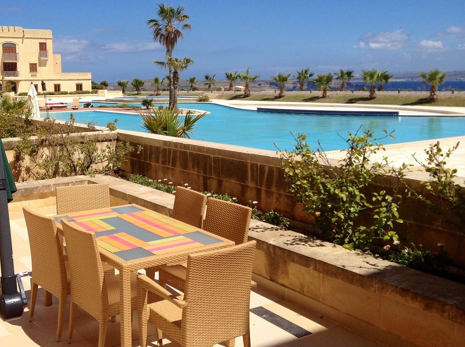 Un espace piscine avec vue sur la mer, des sièges extérieurs et des palmiers.