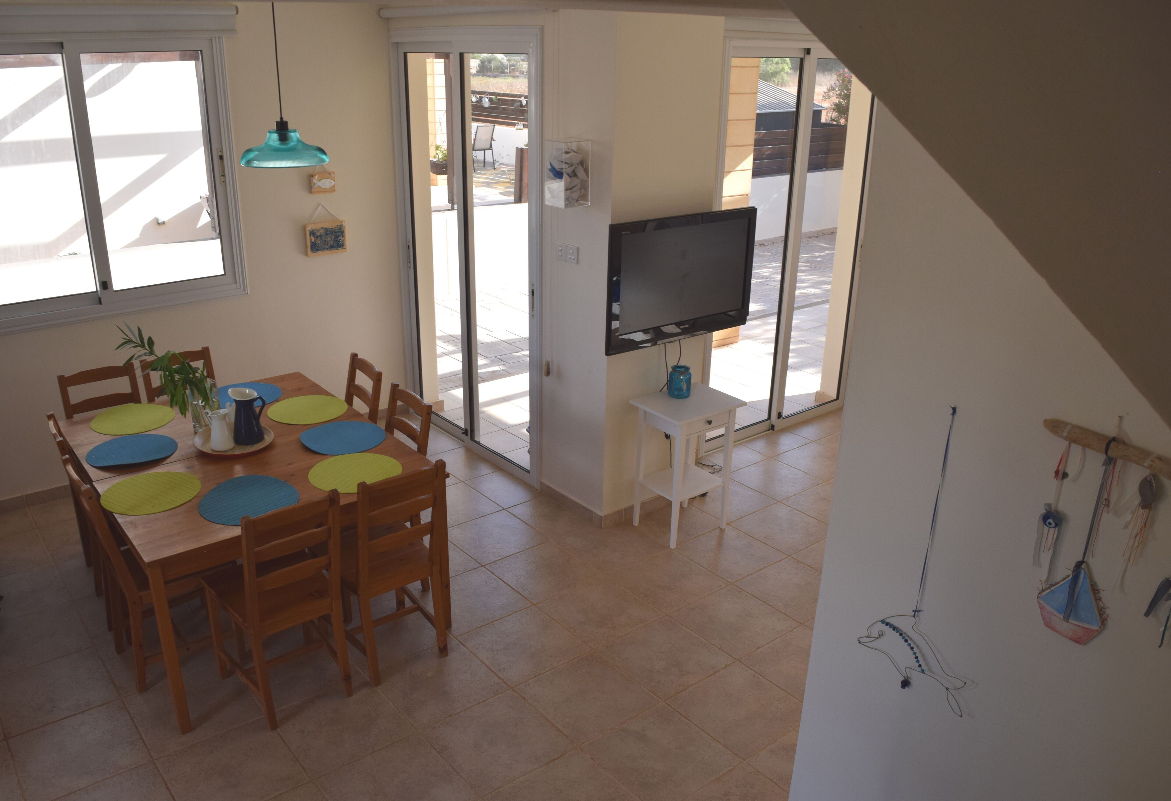 Un'area pranzo con tavolo e sedie, una televisione montata a parete e vista all'esterno tramite una porta scorrevole.