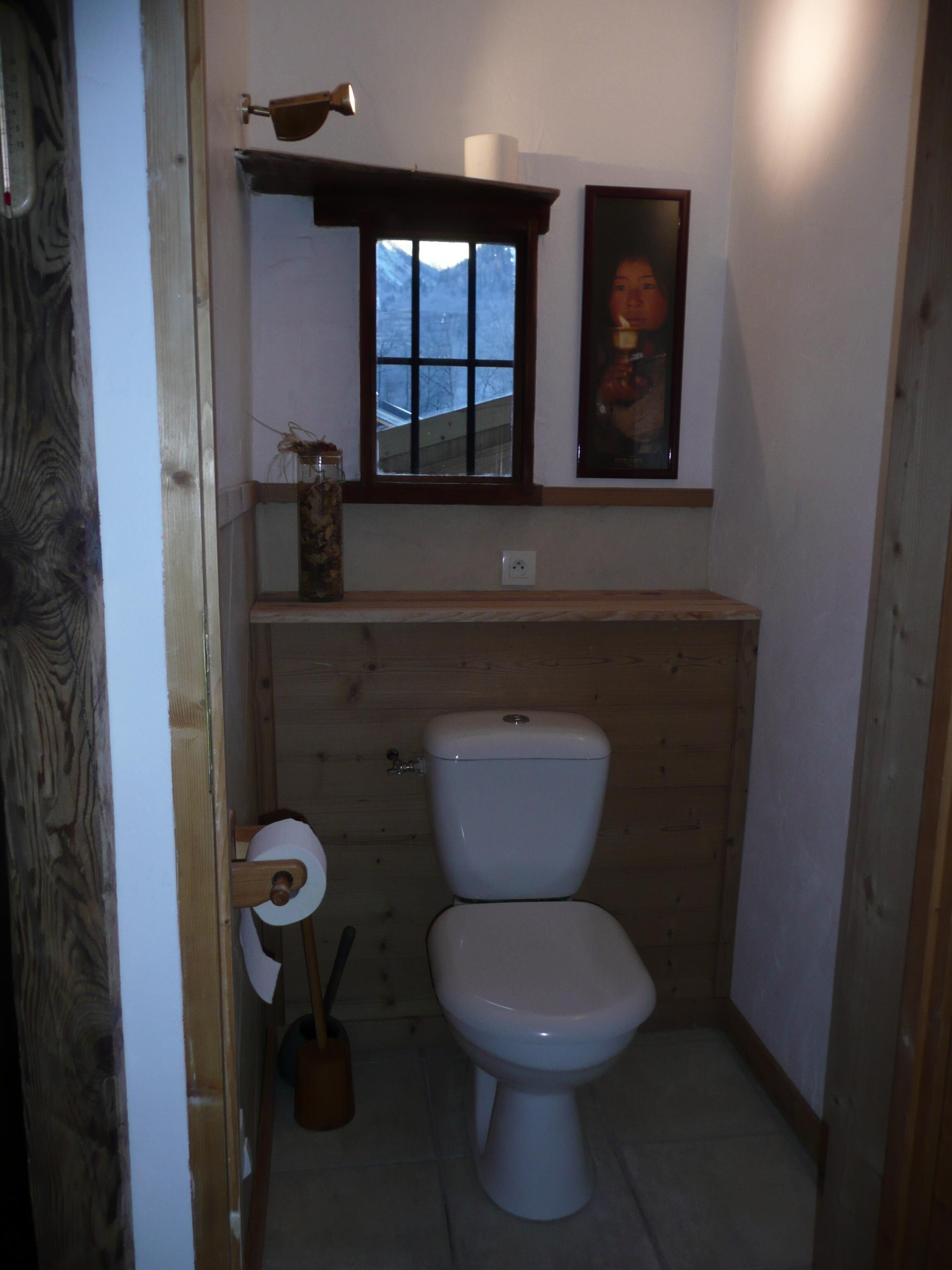 Une petite salle de bain comprenant des toilettes, un meuble-lavabo en bois, une fenêtre et un tableau encadré accroché au mur.