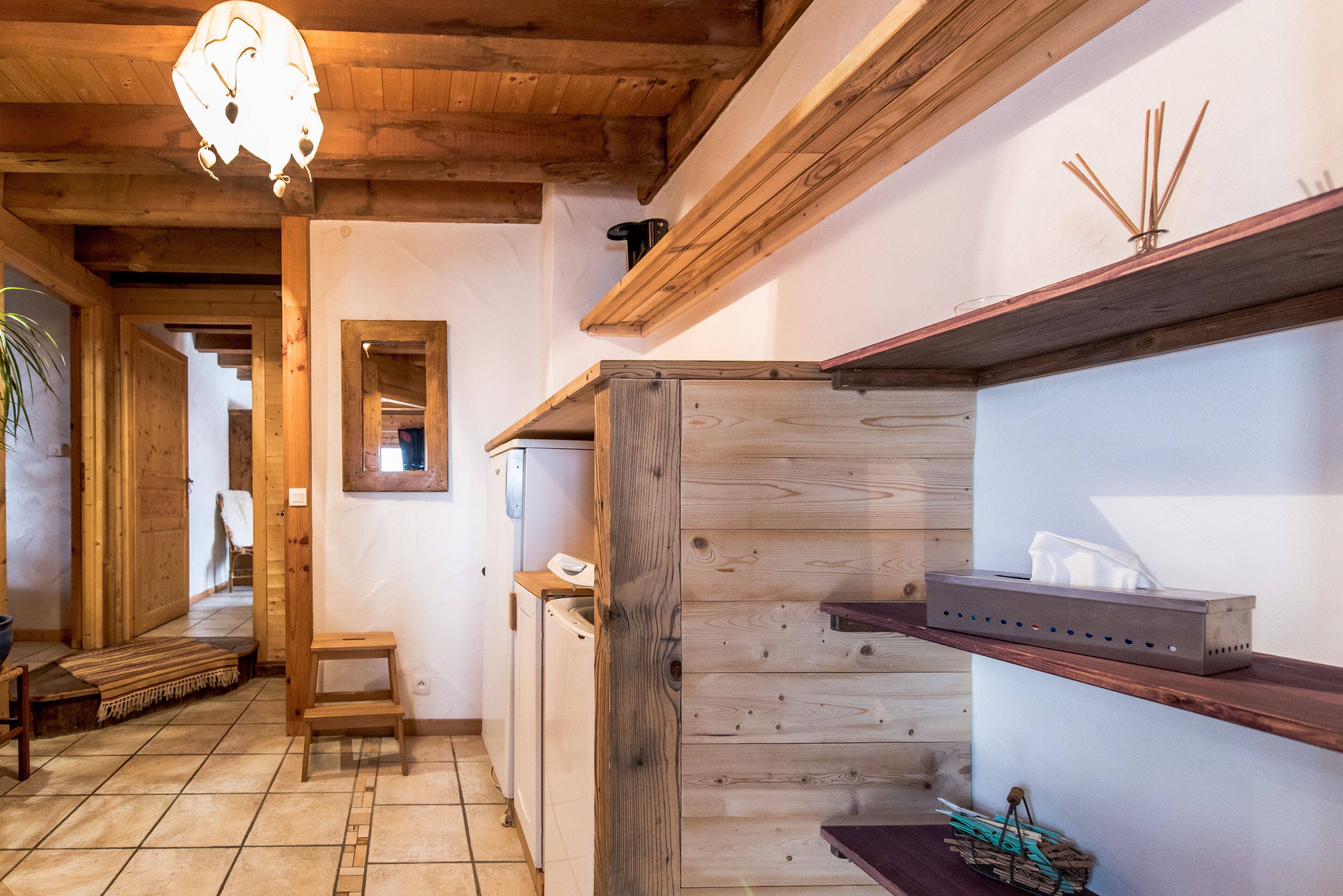 Un interior de madera con techo de madera, un taburete pequeño de madera, un banco de madera, una estantería de madera con una caja de pañuelos y una pared de madera con una ventana.
