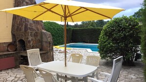 An outdoor patio with a stone table and white plastic chairs, a yellow umbrella, and a stone fireplace. - Secluded house with pool, barbecue and garden 10min. of the beach. Ideal families (Calonge)