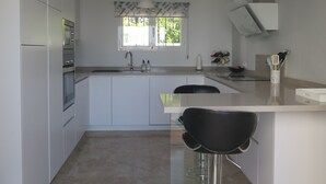 A modern kitchen with white cabinets, a stainless steel refrigerator, a double sink, and a window with patterned curtains. - Casa with Private Pool, Sea Views, Mountain views and Peaceful Location (Nerja)