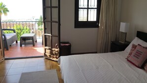 A bedroom with a bed, a nightstand, a window, and an open door leading to a balcony with a table and chairs. - Casa with Private Pool, Sea Views, Mountain views and Peaceful Location (Nerja)