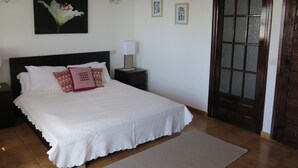A bedroom with a large bed, a nightstand, a lamp, a ceiling fan, a door, and a wall with framed pictures. - Casa with Private Pool, Sea Views, Mountain views and Peaceful Location (Nerja)