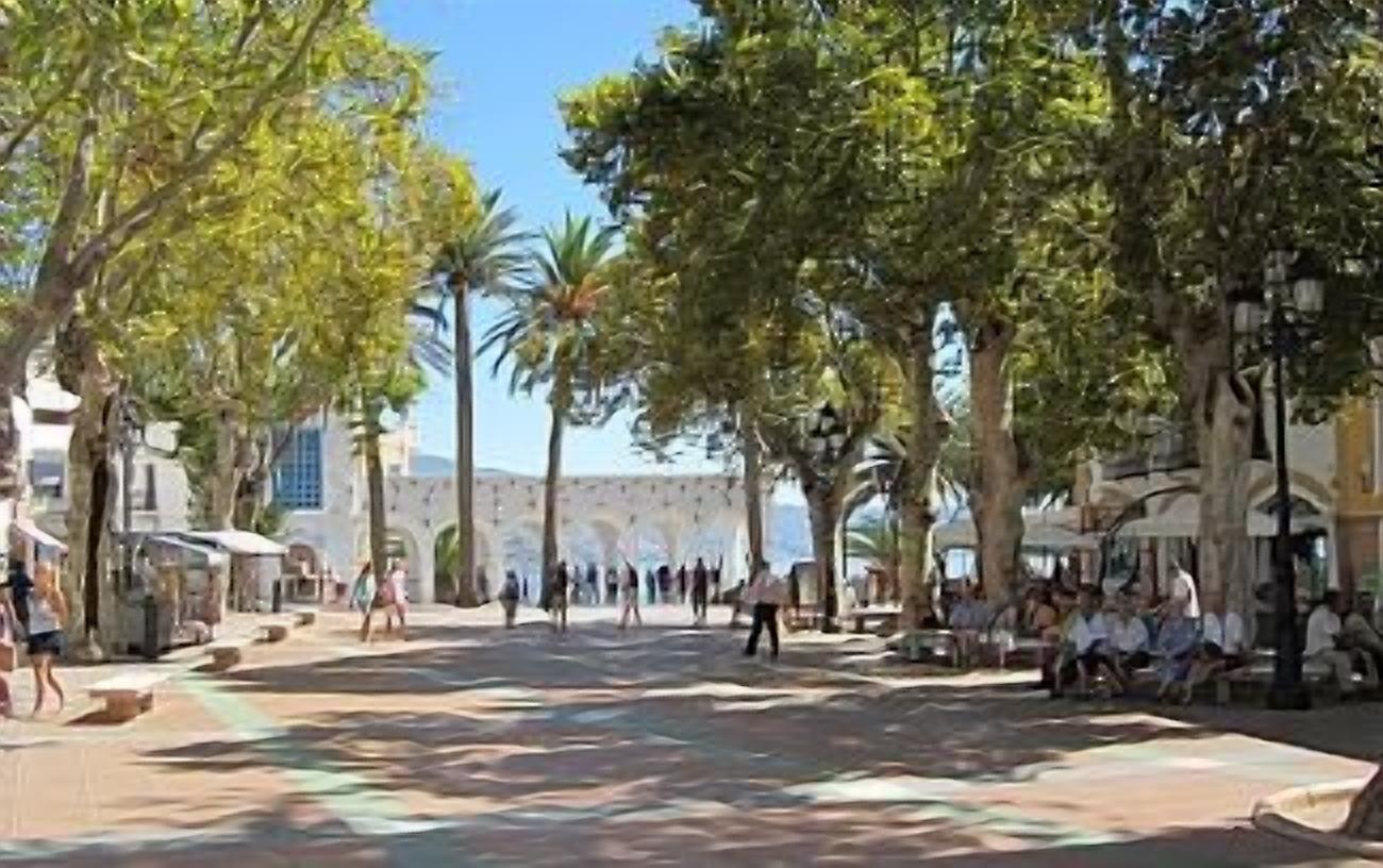 Una plaza pública con árboles, bancos y gente.