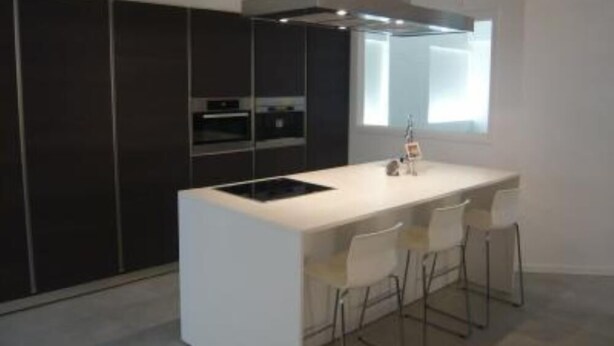 Una cocina moderna con armarios oscuros, una encimera blanca y un horno empotrado.