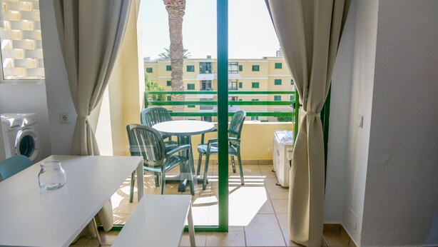 Un balcón con una mesa y sillas, una lavadora y vistas a un edificio con balcones.