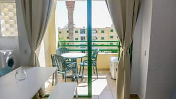 Un balcon avec une table et des chaises, un lave-linge et une vue sur un immeuble doté de balcons.