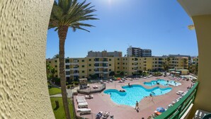 Un resort con una amplia piscina, varias zonas de descanso y vistas de edificios aledaños.