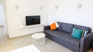 Una sala de estar moderna con un sofá gris, un televisor de pantalla plana sobre un estante blanco y apliques decorativos en la pared.