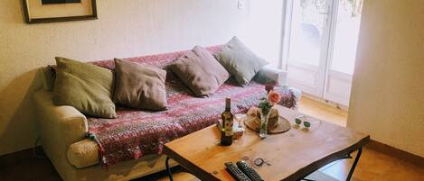A living room with a sofa, a coffee table, and a window with a view of greenery.