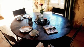 Ett runt matbord med stolar, en kaffekanna, ett vinglas, en bok och en vas med en ros.