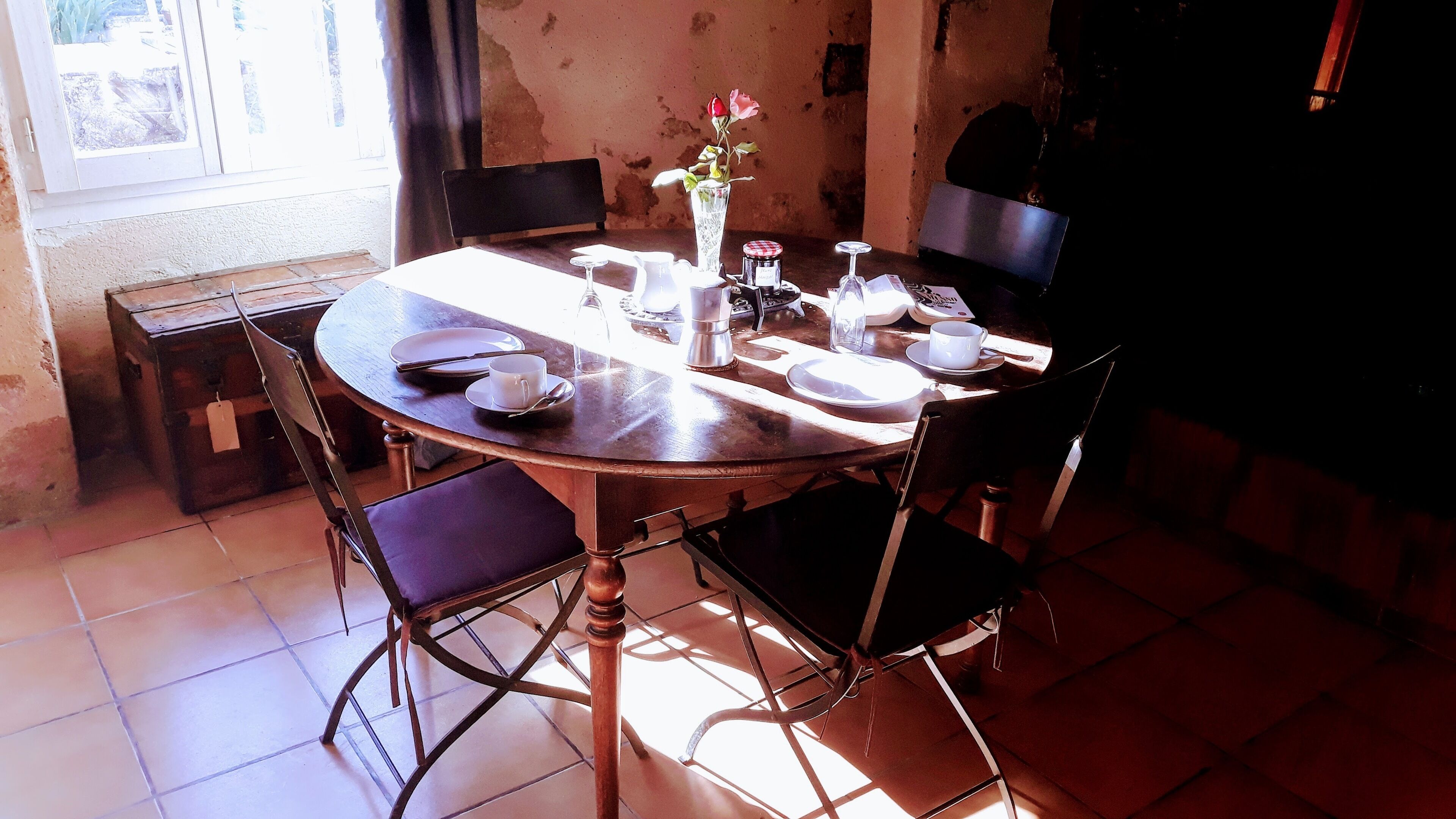 A round dining table with chairs, a vase with flowers, and various tableware.