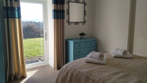 Een slaapkamer met een bed, een dressoir, een spiegel en uitzicht op het landschap.