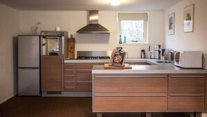 A compact kitchen with a refrigerator, stove, microwave, and wooden cabinets. - Spacious & cozy holiday bungalow "Frank" in wooded area (12 people) (Den Ham)