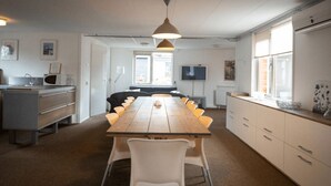 A modern kitchen with a long wooden table, white chairs, and a hanging pendant light. - Spacious & cozy holiday bungalow "Frank" in wooded area (12 people) (Den Ham)