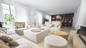 En moderne stue med sofasæt, skrubber og et sofabord. Der er et bogreol og en plante i baggrunden.