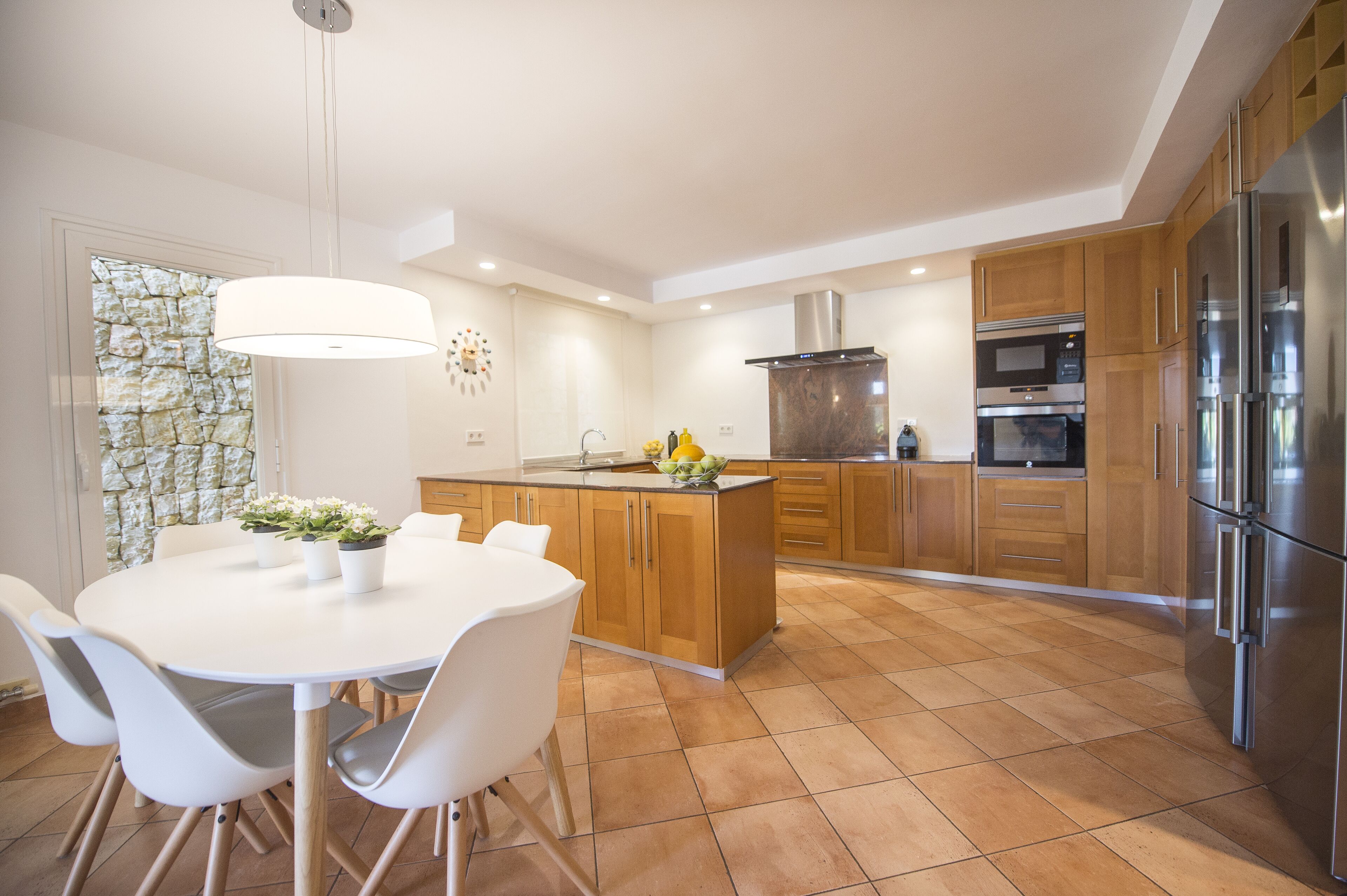 Una cucina moderna con mobili in legno, elettrodomestici in acciaio inossidabile e un tavolo da pranzo bianco con sedie.