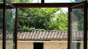 Una habitación con puerta de vidrio que da a un espacio exterior con pared de piedra, techo de tejas y mesa de madera con sillas.