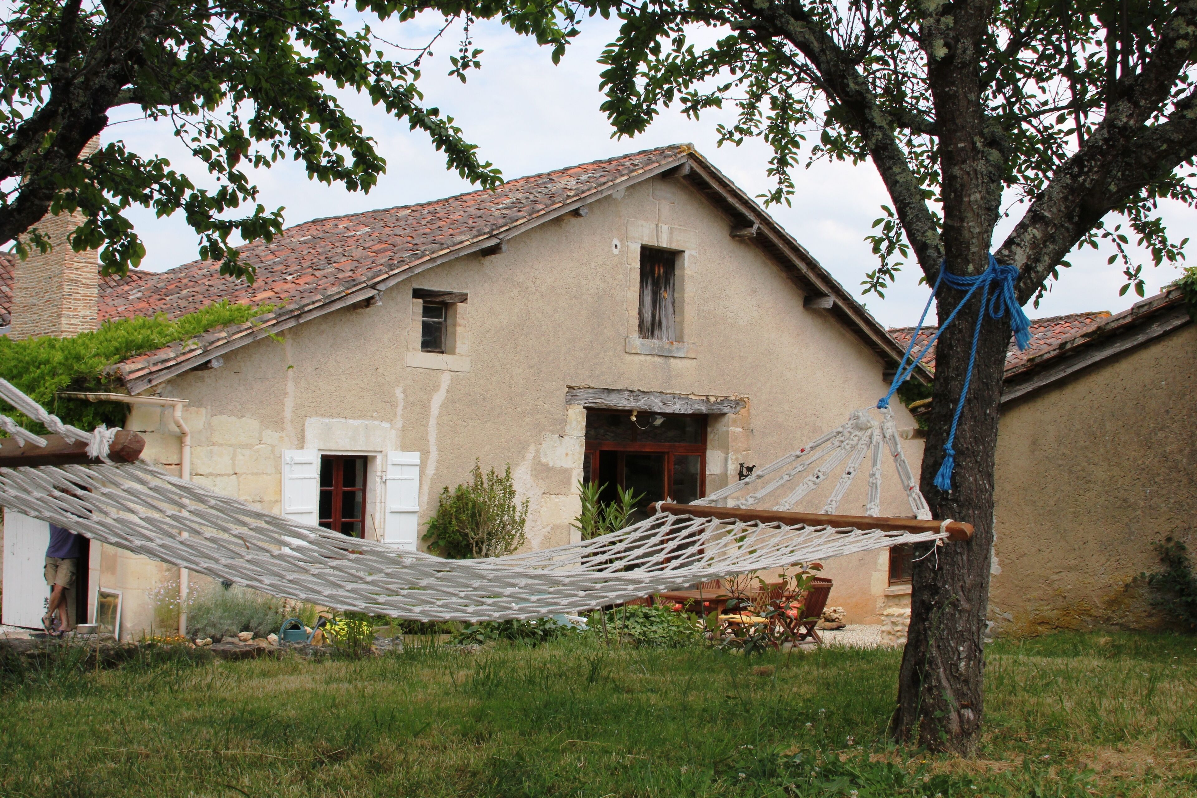 Una casa rústica con una hamaca atada a un árbol, un pequeño porche y un techo de tejas rojas.