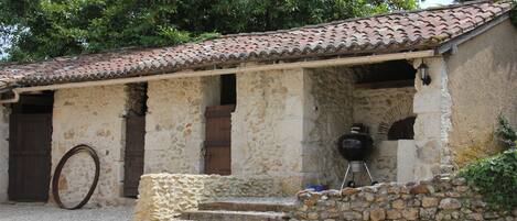 A rustic stone building with a tiled roof, a wooden door, and a grill outside.