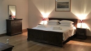 Un dormitorio con techo de madera, una cama con sábanas blancas, dos mesitas de noche con lámparas, un aparador y un cuadro enmarcado en la pared.