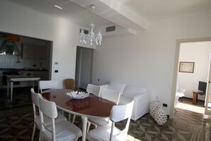 Un comedor con una mesa redonda, sillas blancas y una araña.